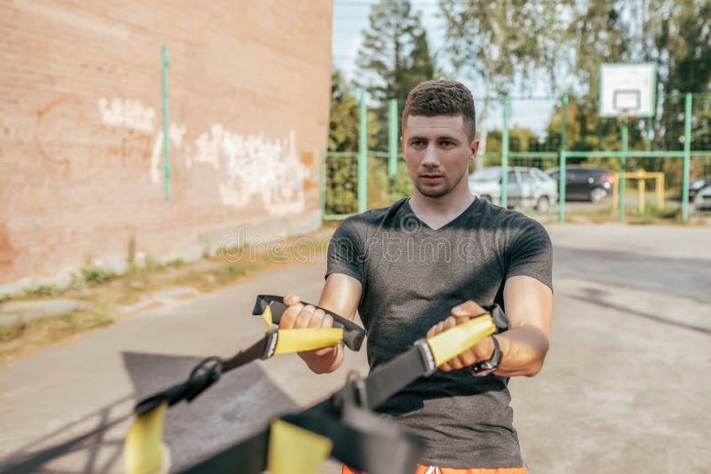 Мужской спортсмен, летом в городе на земле спорт Приниманнсяый за фитнес с резиновыми петлями, ремнями для мышц стоковая фотография rf Мужской спортсмен, летом в городе на земле спорт Приниманнсяый за фитнес с резиновыми петлями, ремнями для мышц стоковая фотография rf