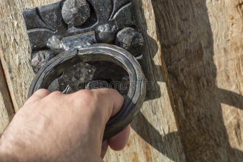 Мужской стук руки с старым черным knocker двери на деревянной и деревенской двери стоковые фотографии rf Мужской стук руки с старым черным knocker двери на деревянной и деревенской двери стоковые фотографии rf