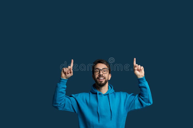 A man wearing a blue hoodie is standing with his hands raised in the air. He appears to be in a position of surrender or submission, copy space. A man wearing a blue hoodie is standing with his hands raised in the air. He appears to be in a position of surrender or submission, copy space