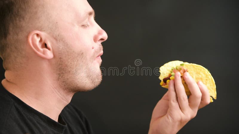 мужчина ест вегетарианский тако с овощами. молодой человек ест мексиканскую еду на черном фоне