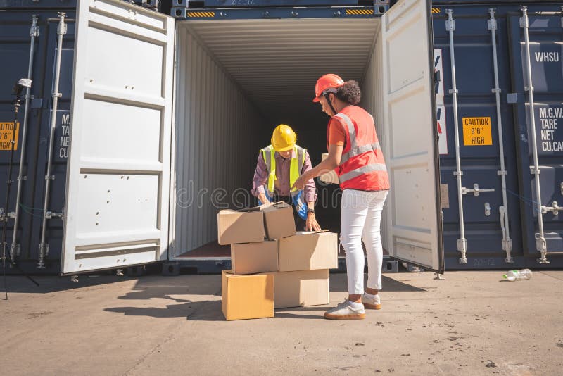 2 workers, Asian men and African woman, holding and helping checking boxes to be transported into the container, to worker and transport in the export industry concept. 2 workers, Asian men and African woman, holding and helping checking boxes to be transported into the container, to worker and transport in the export industry concept