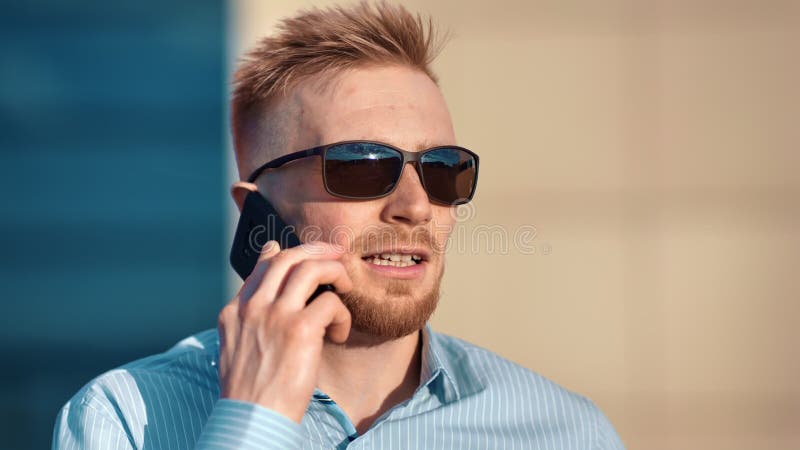 Мужчина стороны конца-вверх уверенный успешный бородатый в солнечных очках обсуждая дело используя смартфон