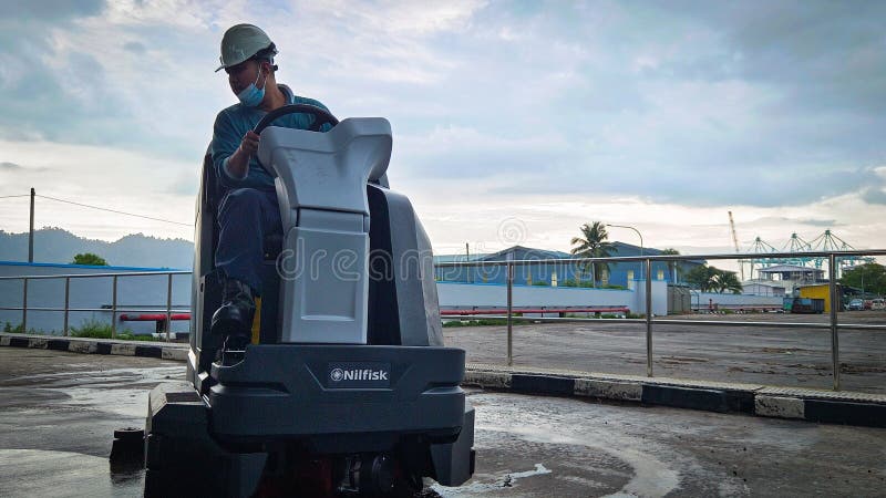 Lumut, Perak - April 2 2024: A man is cleaning a cement floor using a floor cleaning machine in a cemented area in a factory. Lumut, Perak - April 2 2024: A man is cleaning a cement floor using a floor cleaning machine in a cemented area in a factory.