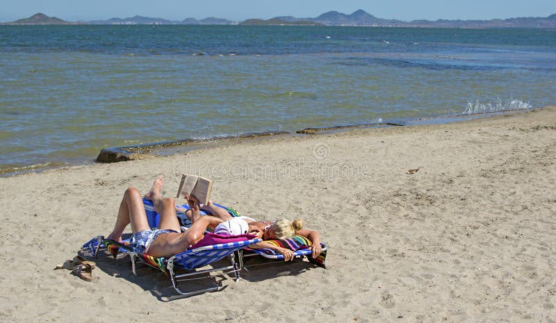 Мурсия, Испания - 22-ое июня 2019: Счастливые пары читая книгу и ослабляя на пляже во время солнечного летнего дня стоковые фото Мурсия, Испания - 22-ое июня 2019: Счастливые пары читая книгу и ослабляя на пляже во время солнечного летнего дня стоковые фото