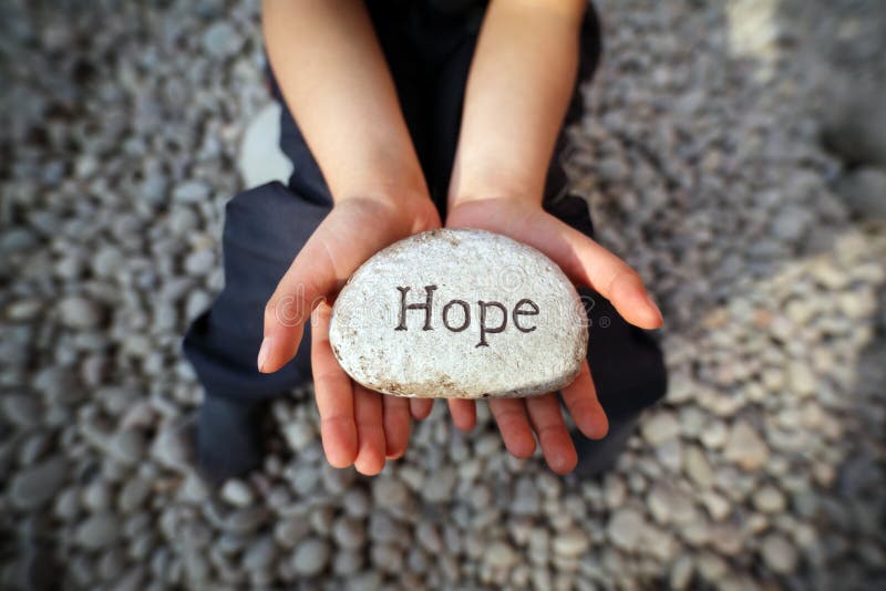 Child on a beach with hands cupped holding stone pebble with the word hope engraved concept for faith, love, spirituality and religion. Child on a beach with hands cupped holding stone pebble with the word hope engraved concept for faith, love, spirituality and religion