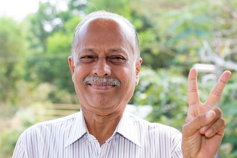 Closeup portrait, joyful elderly gentleman in white striped shirt holding up two fingers, isolated outside outdoors background. Closeup portrait, joyful elderly gentleman in white striped shirt holding up two fingers, isolated outside outdoors background