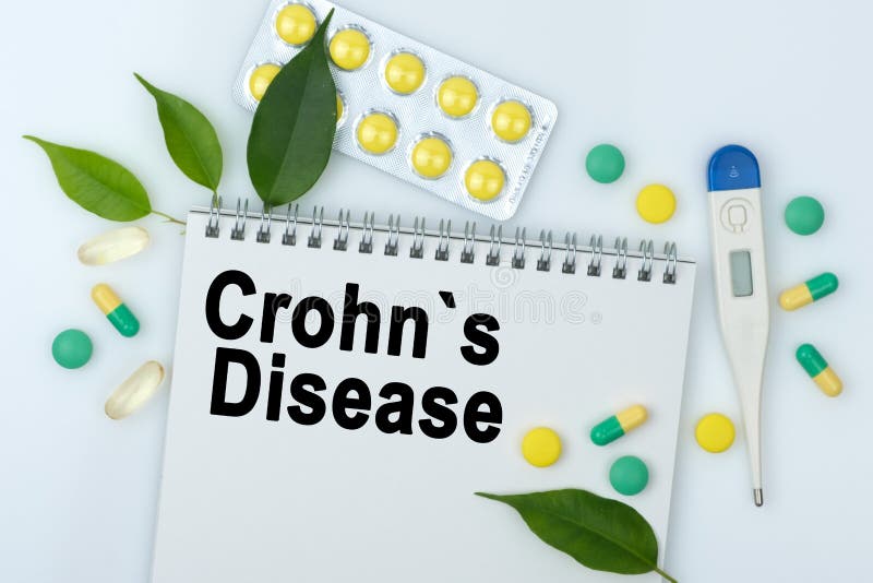 На столе таблетки листья градусника и ноутбук с болезнью crohns надписи стоковые фото