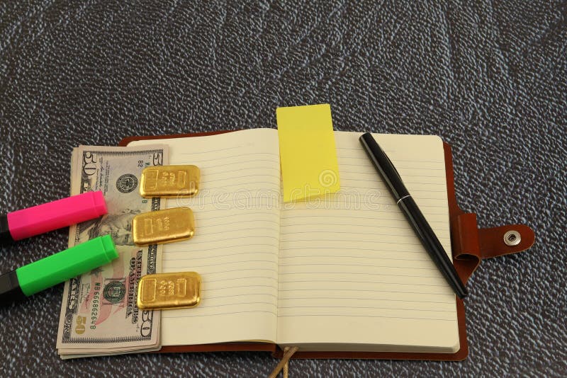 On the table is a notebook, gold bars and cash dollars. Foreground.Color markers. On the table is a notebook, gold bars and cash dollars. Foreground.Color markers.