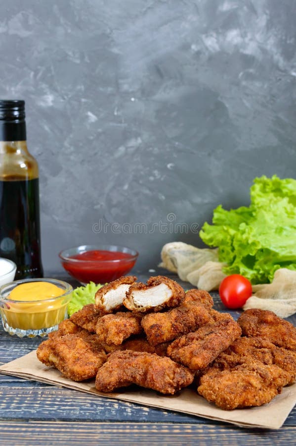 Наггеты цыпленка Части глубок-зажаренного кудрявого мяса, на бумаге с различными соусами на деревянном столе стоковые фото