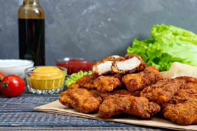 Наггеты цыпленка Части глубок-зажаренного кудрявого мяса, на бумаге с различными соусами на деревянном столе стоковое фото