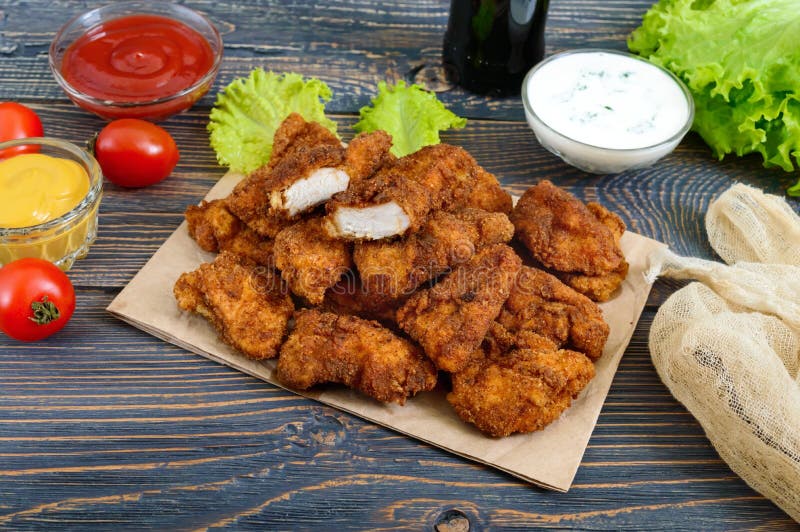 Наггеты цыпленка Части глубок-зажаренного кудрявого мяса, на бумаге с различными соусами на деревянном столе стоковые фото
