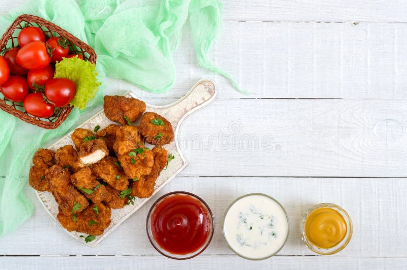 Наггеты цыпленка Части глубок-зажаренного кудрявого мяса, на бумаге с различными соусами на белом деревянном столе стоковое изображение
