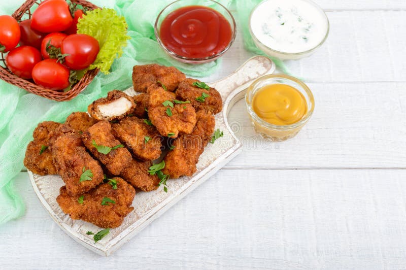 Наггеты цыпленка Части глубок-зажаренного кудрявого мяса, на бумаге с различными соусами стоковые фото