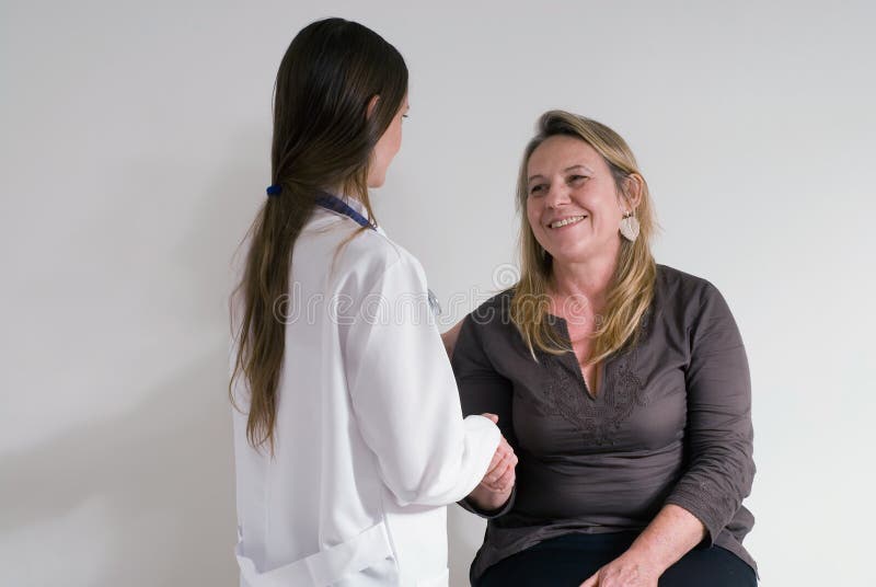 An isolated shot of a doctor/nurse and her female patient smiling and shaking hands. An isolated shot of a doctor/nurse and her female patient smiling and shaking hands.