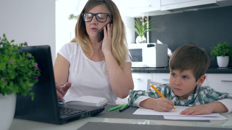 Надомный труд, мать говорит на мобильном телефоне пока сын играет около ее