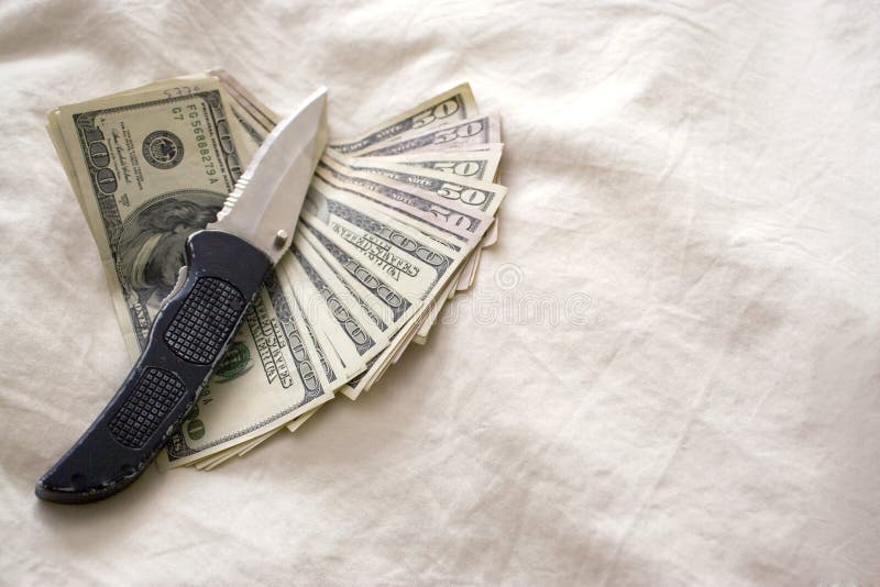 A knife and some fanned out cash laying on a bed. A knife and some fanned out cash laying on a bed.