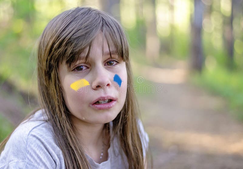 напуганный ребёнок плачет один в лесу. знак украинского флага на щеке детей. мировой кризис украинской геополитики. стоковые фото