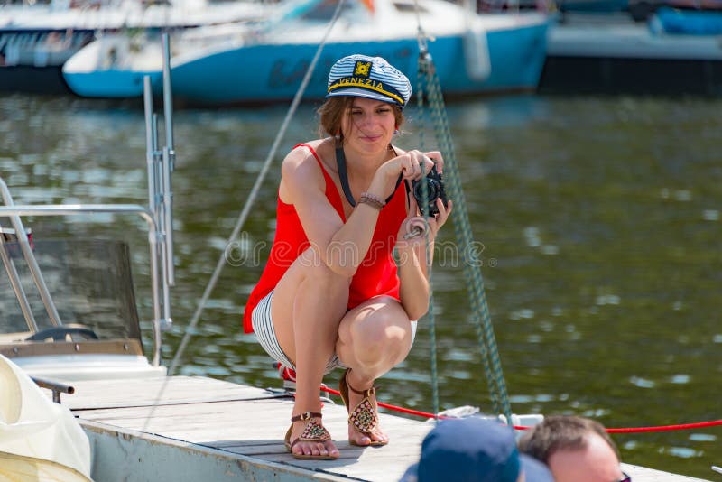 Summer mood: a girl taking pictures at the yacht club. On a clear Sunny weekends, many people spend time on the water at the yacht clubs, riding on boats, catch the wind in the sails. One of the visitors - a young woman in a red dress and a white sailor's cap on, taking pictures of their friends in the boat. Summer mood: a girl taking pictures at the yacht club. On a clear Sunny weekends, many people spend time on the water at the yacht clubs, riding on boats, catch the wind in the sails. One of the visitors - a young woman in a red dress and a white sailor's cap on, taking pictures of their friends in the boat.