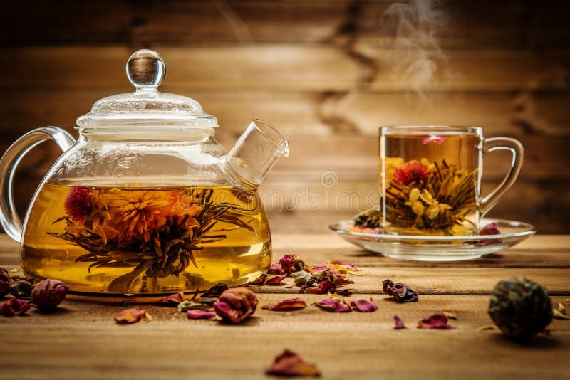 Teapot and glass cup with blooming tea flower inside against wooden background. Teapot and glass cup with blooming tea flower inside against wooden background