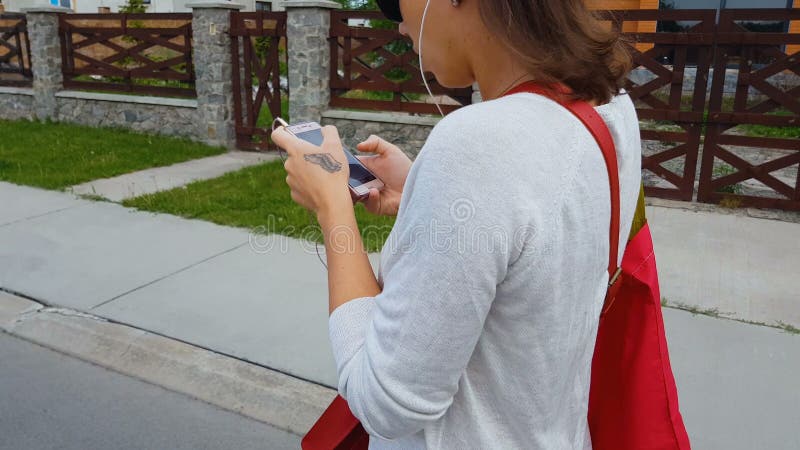 Наушники студентки смотря в приложении смартфона, идя улице, опасности жизни