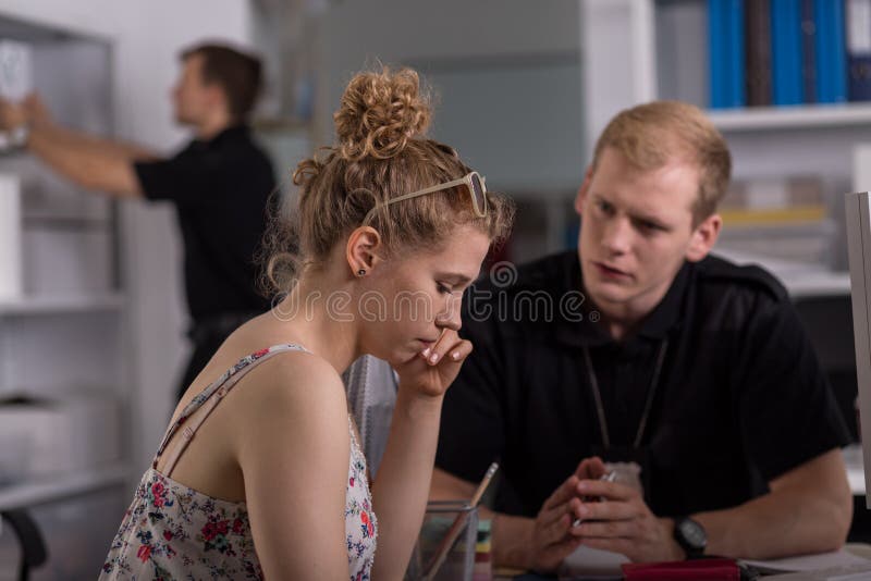 Shot of a sad young women sitting at a police station with a young policeman. Shot of a sad young women sitting at a police station with a young policeman