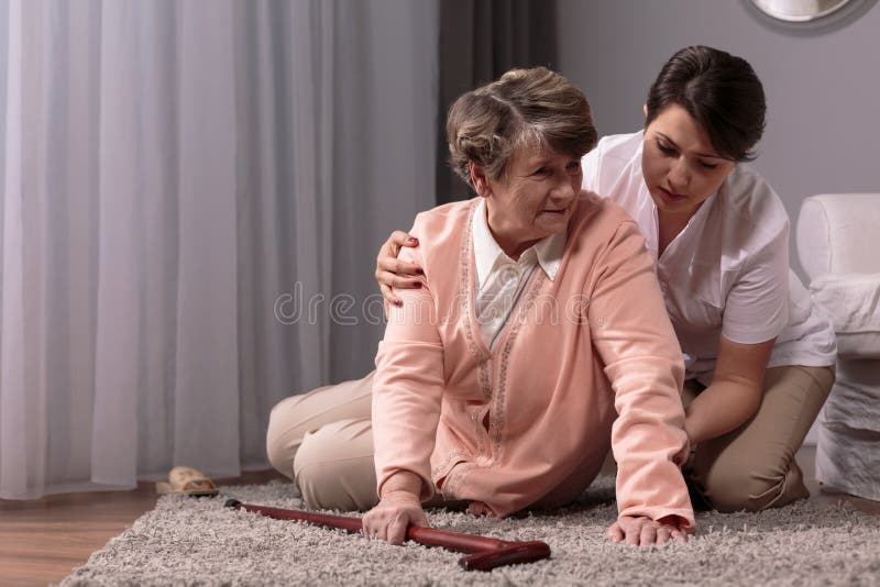 Carer helping senior women with walking stick to stand up from floor. Carer helping senior women with walking stick to stand up from floor.