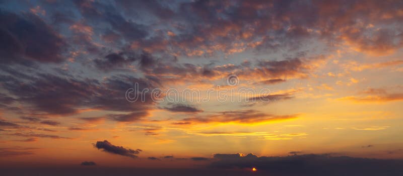 Небо во время красочного, яркого оранжевого захода солнца, лучей солнца делает их путь через облака