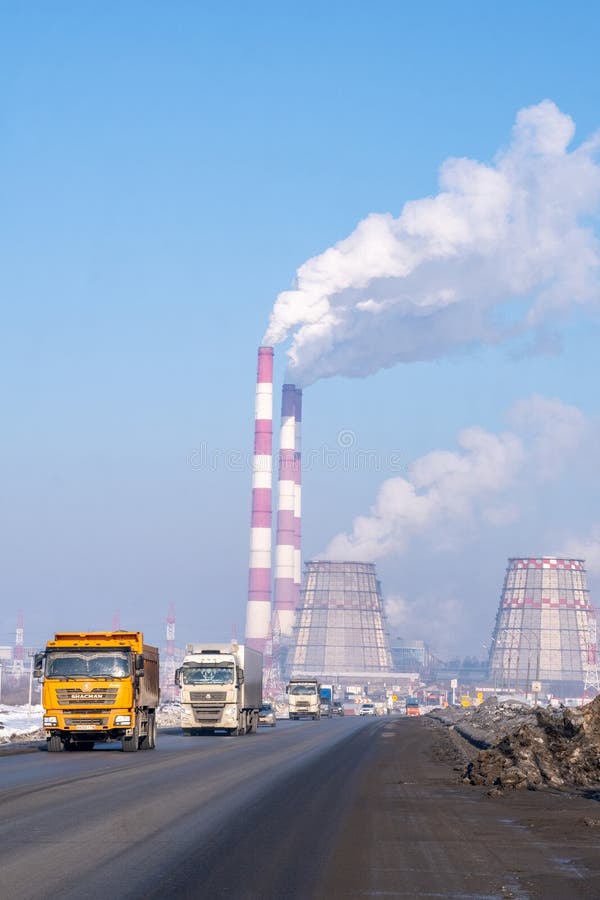 Naberezhnye Chelny, Russia, March 2, 2024. A factory with smoke billowing from its chimneys against the cloudy sky, as vehicles pass by on the asphalt road, reflecting in automotive sideview mirrors. Naberezhnye Chelny, Russia, March 2, 2024. A factory with smoke billowing from its chimneys against the cloudy sky, as vehicles pass by on the asphalt road, reflecting in automotive sideview mirrors