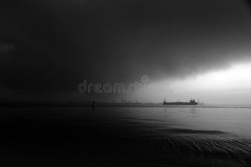 Sail into ocean storm waters - A dramatic nature landscape picture of a ship vessel sailing headlong into pitch dark stormy rain thunder clouds that cover almost the whole skies. Calm before impending tropical storm. Hints of coming hurricane and gales. Composed with copy space for text, words, etc. A monochrome bw image. Concept and metaphoric image for determination, facing and taking on adversity, steadfastness, etc. Black and white moody photograph, simple composition with copy space. Sail into ocean storm waters - A dramatic nature landscape picture of a ship vessel sailing headlong into pitch dark stormy rain thunder clouds that cover almost the whole skies. Calm before impending tropical storm. Hints of coming hurricane and gales. Composed with copy space for text, words, etc. A monochrome bw image. Concept and metaphoric image for determination, facing and taking on adversity, steadfastness, etc. Black and white moody photograph, simple composition with copy space.