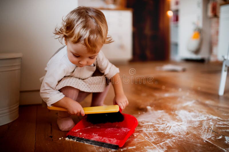 Небольшая девушка малыша с полом уборки щетки и dustpan в кухне дома стоковые изображения Небольшая девушка малыша с полом уборки щетки и dustpan в кухне дома стоковые изображения