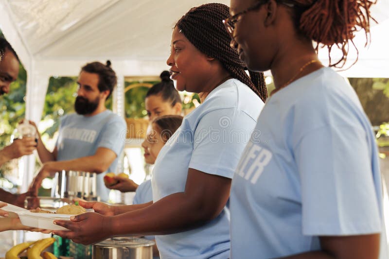 Voluntary multiethnic people distributes needed products and free meals to the hungry, demonstrating charity in aiding the less privileged. Non-profit outdoor food bank serving hot food to the needy. Voluntary multiethnic people distributes needed products and free meals to the hungry, demonstrating charity in aiding the less privileged. Non-profit outdoor food bank serving hot food to the needy.