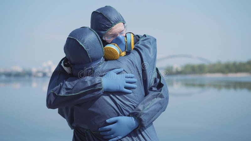 Непознаваемая женщина в химическом костюме приходит к молодому любящему человеку в респираторе и защитных очков на открытом воздух сток-видео