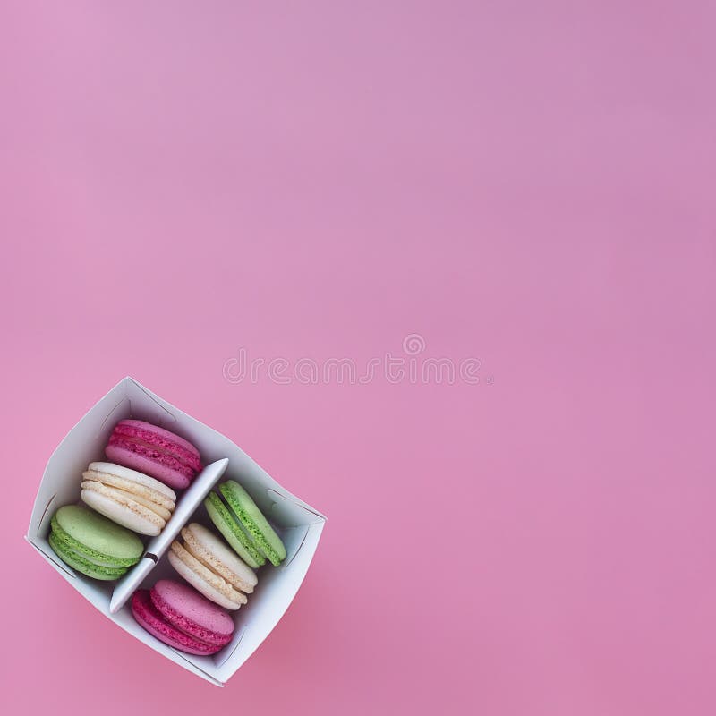 Несколько пестротканых macarons в бумажной коробке на квадратной розовой предпосылке стоковая фотография rf Несколько пестротканых macarons в бумажной коробке на квадратной розовой предпосылке стоковая фотография rf