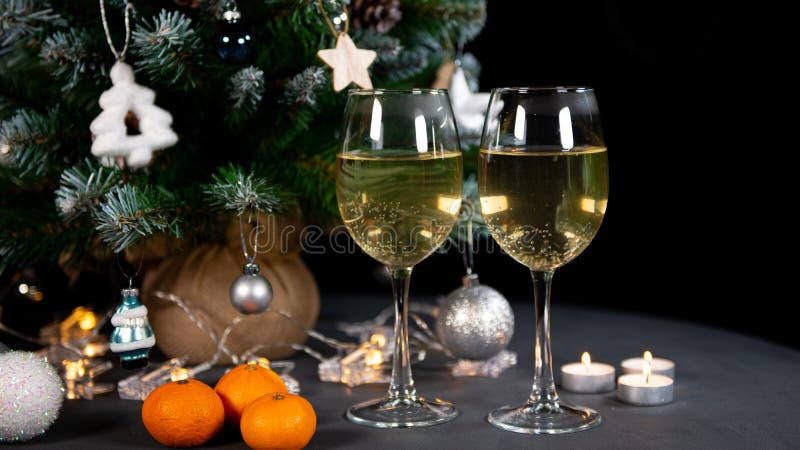 New year`s still life, 2 glasses of champagne tangerines on the table on the background of the Christmas tree. black background. New year`s still life, 2 glasses of champagne tangerines on the table on the background of the Christmas tree. black background