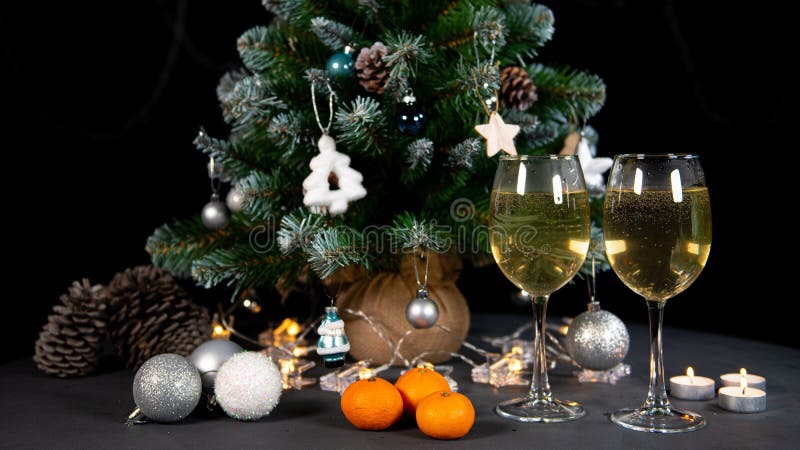 New year`s still life, 2 glasses of champagne tangerines on the table on the background of the Christmas tree. black background. New year`s still life, 2 glasses of champagne tangerines on the table on the background of the Christmas tree. black background