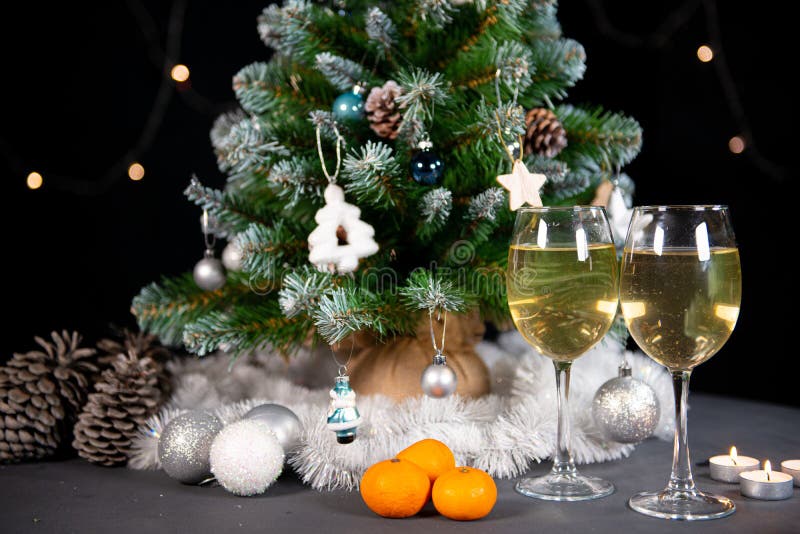 New year`s still life, 2 glasses of champagne tangerines on the table on the background of the Christmas tree. black background. New year`s still life, 2 glasses of champagne tangerines on the table on the background of the Christmas tree. black background