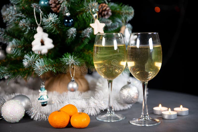 New year`s still life, 2 glasses of champagne tangerines on the table on the background of the Christmas tree. black background. New year`s still life, 2 glasses of champagne tangerines on the table on the background of the Christmas tree. black background