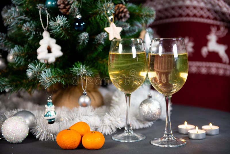 New year`s still life, 2 glasses of champagne tangerines on the table on the background of the Christmas tree. black background. New year`s still life, 2 glasses of champagne tangerines on the table on the background of the Christmas tree. black background