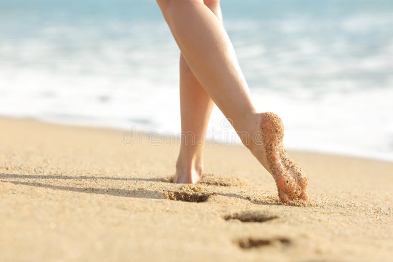 Woman legs and feet walking on the sand of the beach with the sea water in the background. Woman legs and feet walking on the sand of the beach with the sea water in the background