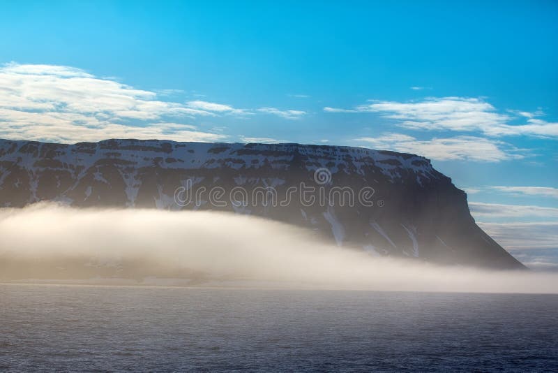 Gloomy Cover glacier in Arctic ( Franz-Josef Land, Northbrook island). Cloud caught on the glacial sheet. Clouds slide over from glacier and cliff to sea. Gloomy Cover glacier in Arctic ( Franz-Josef Land, Northbrook island). Cloud caught on the glacial sheet. Clouds slide over from glacier and cliff to sea