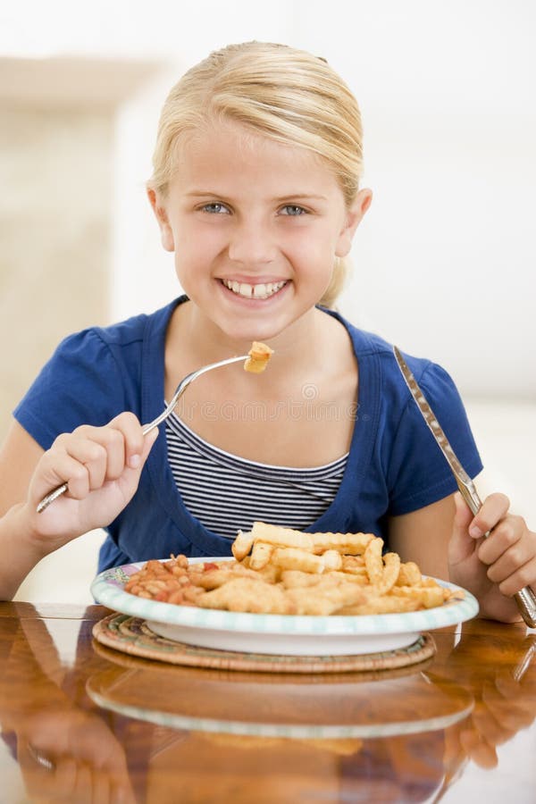 Young girl indoors eating fish and chips smiling. Young girl indoors eating fish and chips smiling