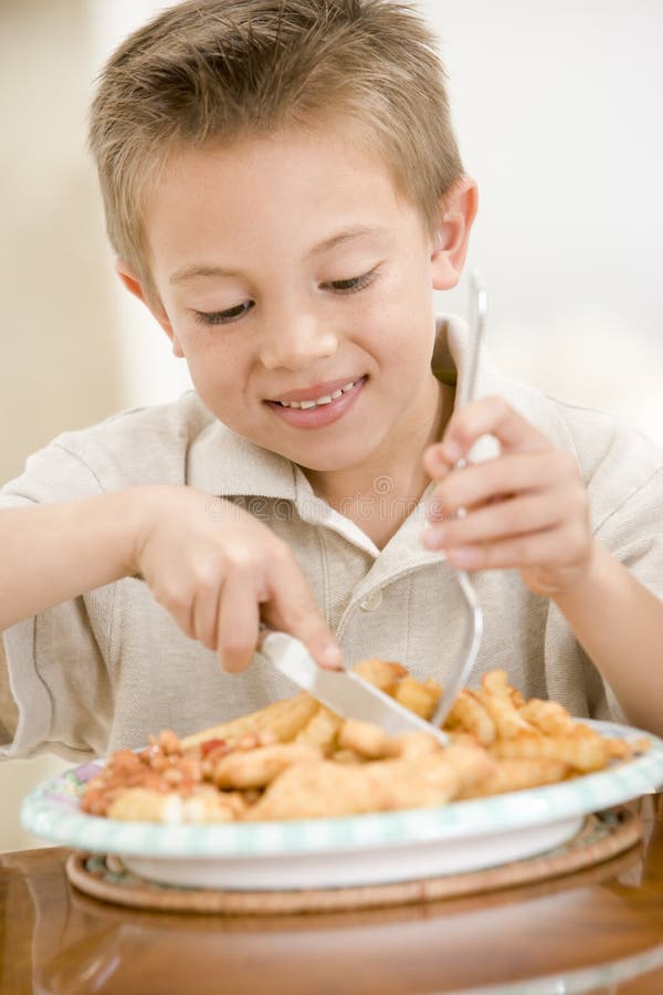 Young boy indoors eating fish and chips smiling. Young boy indoors eating fish and chips smiling