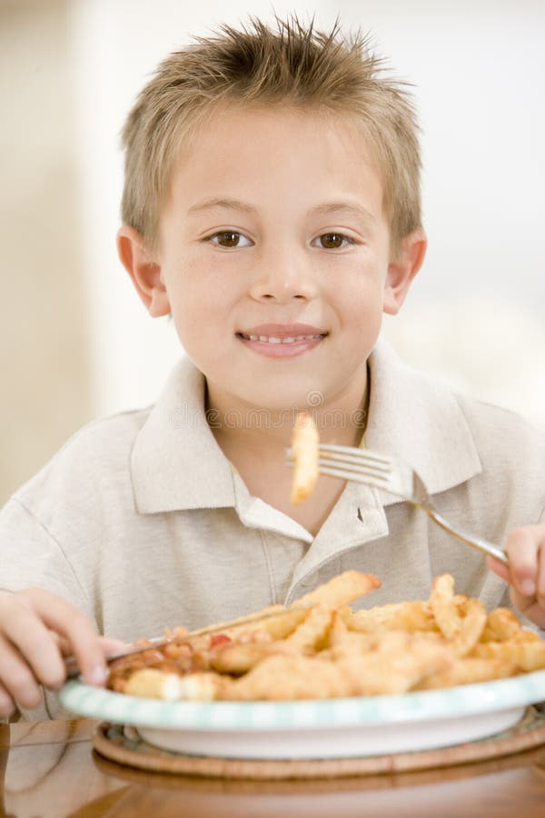 Young boy indoors eating fish and chips smiling. Young boy indoors eating fish and chips smiling