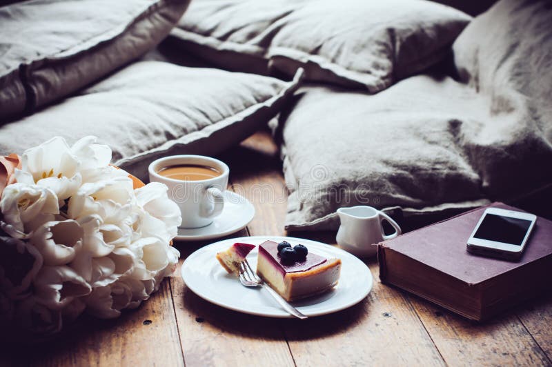 Pillows, a bouquet of tulips, coffee with milk, cheesecake and smartphone on a shabby wooden floor. Hipster lifestyle. Pillows, a bouquet of tulips, coffee with milk, cheesecake and smartphone on a shabby wooden floor. Hipster lifestyle