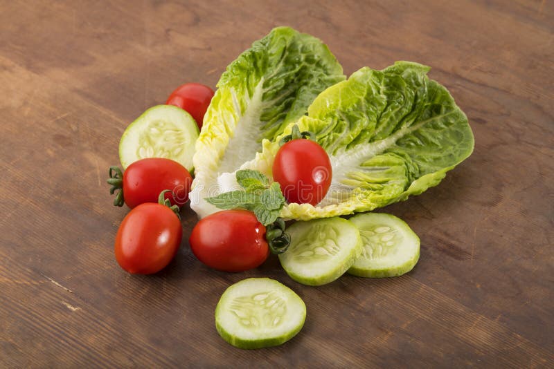 Овощ: Свежий зеленый салат Romaine с томатами младенца, листьями мяты и кусками огурца на предпосылке Брайна деревянной стоковое фото rf Овощ: Свежий зеленый салат Romaine с томатами младенца, листьями мяты и кусками огурца на предпосылке Брайна деревянной стоковое фото rf