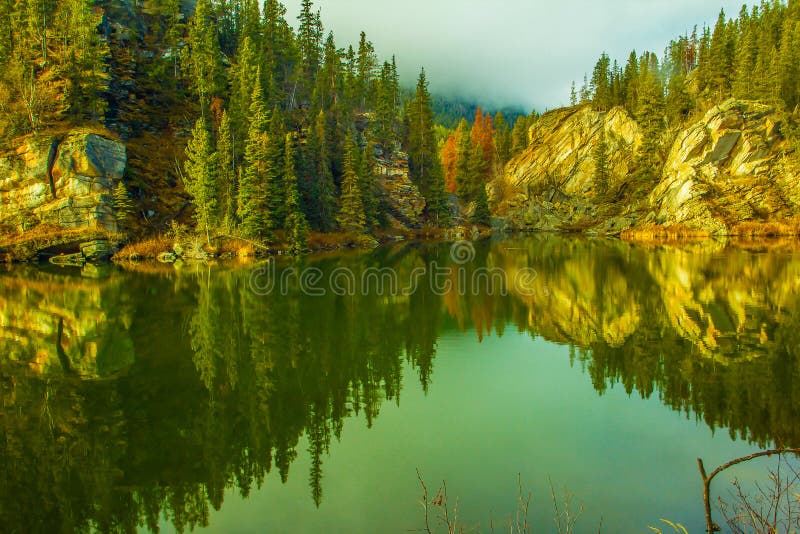 Rocks and pines in fall colours are reflected into yellowhead lake. Rocks and pines in fall colours are reflected into yellowhead lake