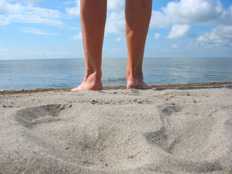 There are sand, legs, footprints, clouds, sly, skyline and lake. There are sand, legs, footprints, clouds, sly, skyline and lake