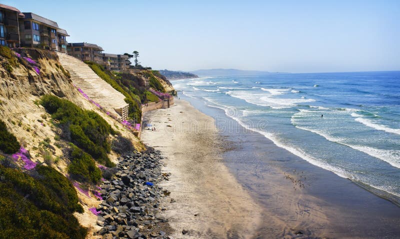 Residentail buildings, mostly condominiums, are precariously built on eroding cliffs, strengthened and reinforced with rocks and concrete walls, over the beach and Pacific Ocean in Solana Beach, southern California, San Diego County, with vibrant pink flowers brightly blooming on a blue sky day, in an area known as North County, popular with tourists and locals for recreational water activities. Residentail buildings, mostly condominiums, are precariously built on eroding cliffs, strengthened and reinforced with rocks and concrete walls, over the beach and Pacific Ocean in Solana Beach, southern California, San Diego County, with vibrant pink flowers brightly blooming on a blue sky day, in an area known as North County, popular with tourists and locals for recreational water activities.