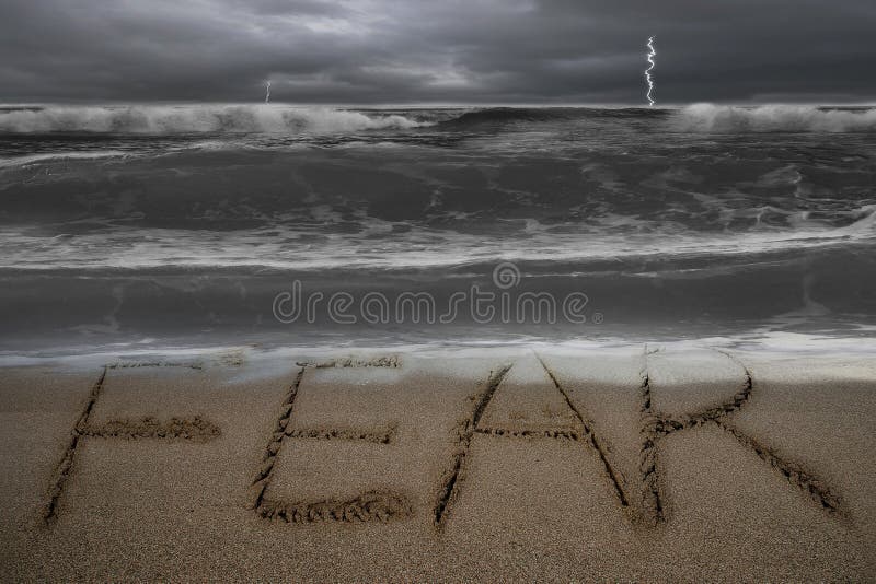 Fear word hand written on sand beach with dark stormy ocean background. Fear word hand written on sand beach with dark stormy ocean background