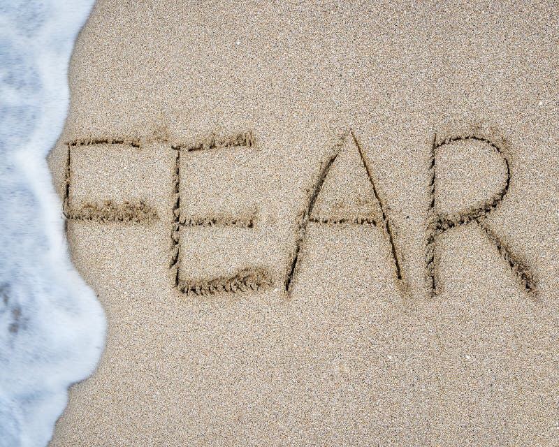 Fear word hand written with white wave foam on sand beach background. Fear word hand written with white wave foam on sand beach background